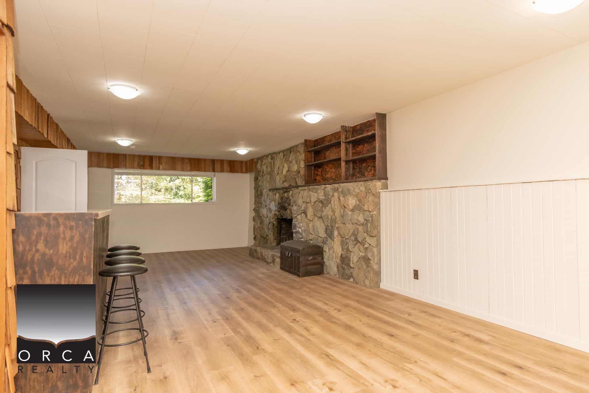 Bright spacious living room with stone fireplace, hardwood floors, and large window showcasing natural light, perfect for relaxing and entertaining in a cozy home setting.