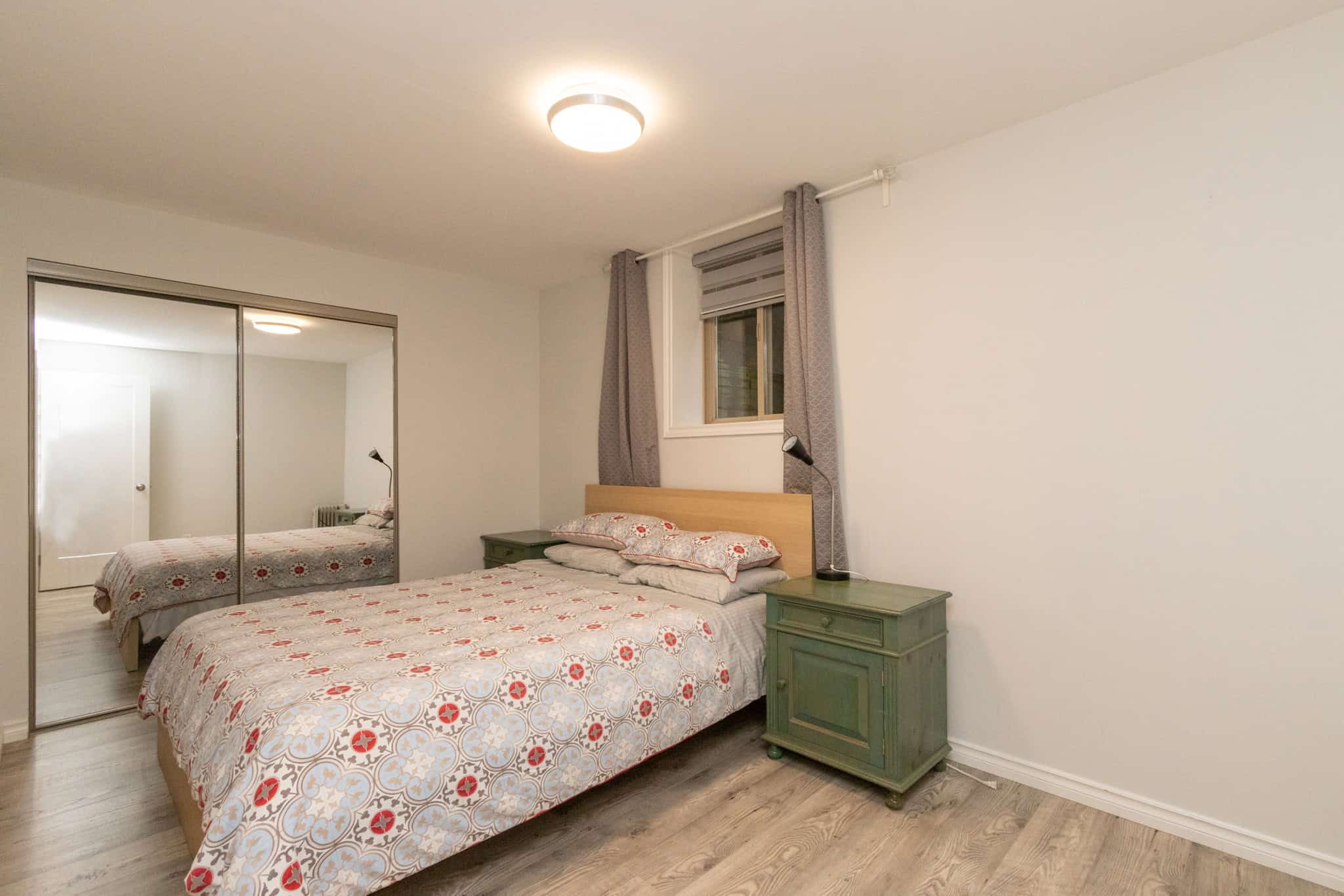 32 Bright bedroom in Vancouver featuring a double bed, green nightstands, large mirrored closet, and a window with grey curtains - perfect for homebuyers seeking real estate in BC.