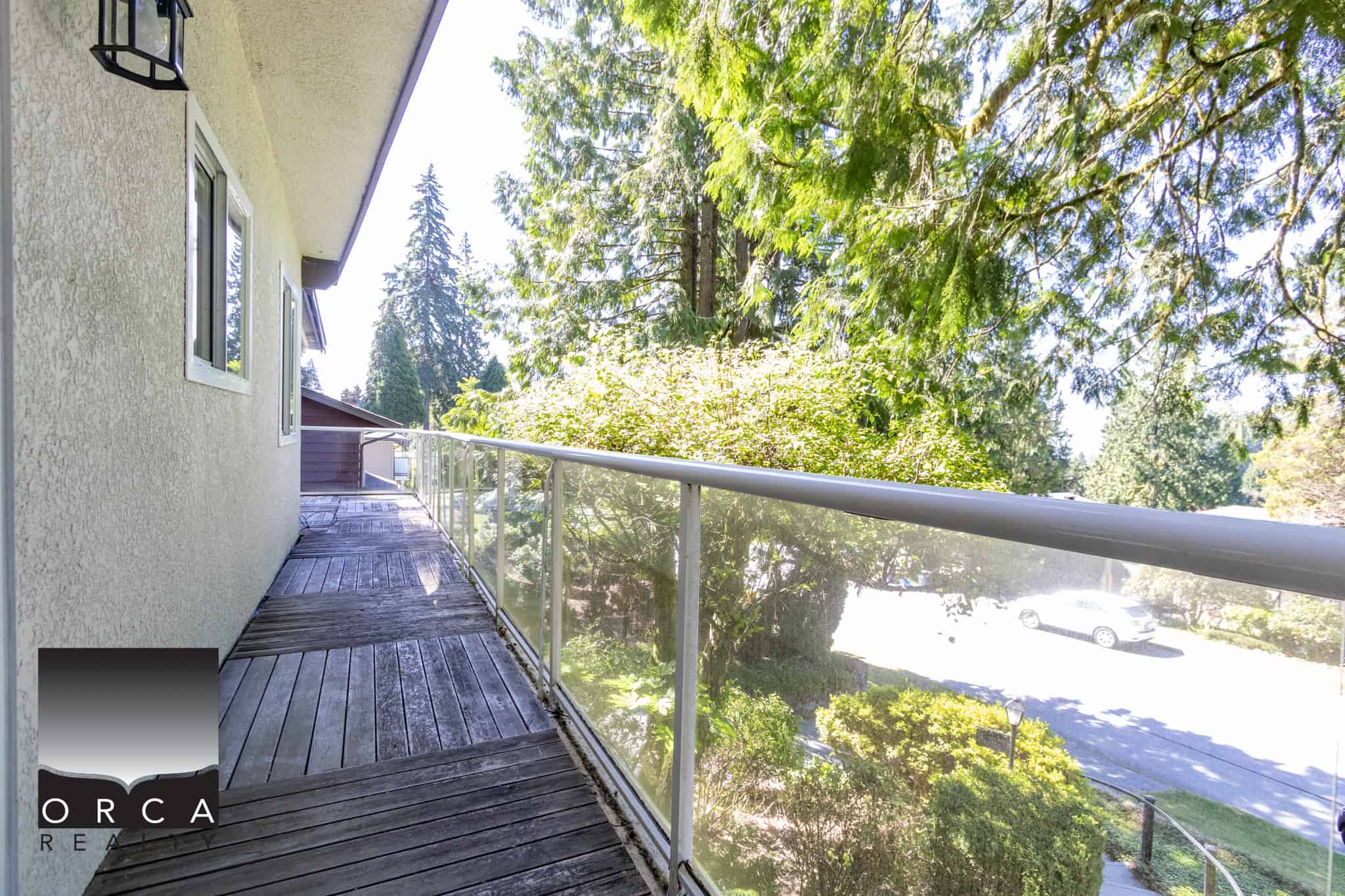 Peaceful balcony with glass railing overlooking lush greenery and parking area, ideal for relaxing and enjoying outdoor views in a residential or real estate setting.