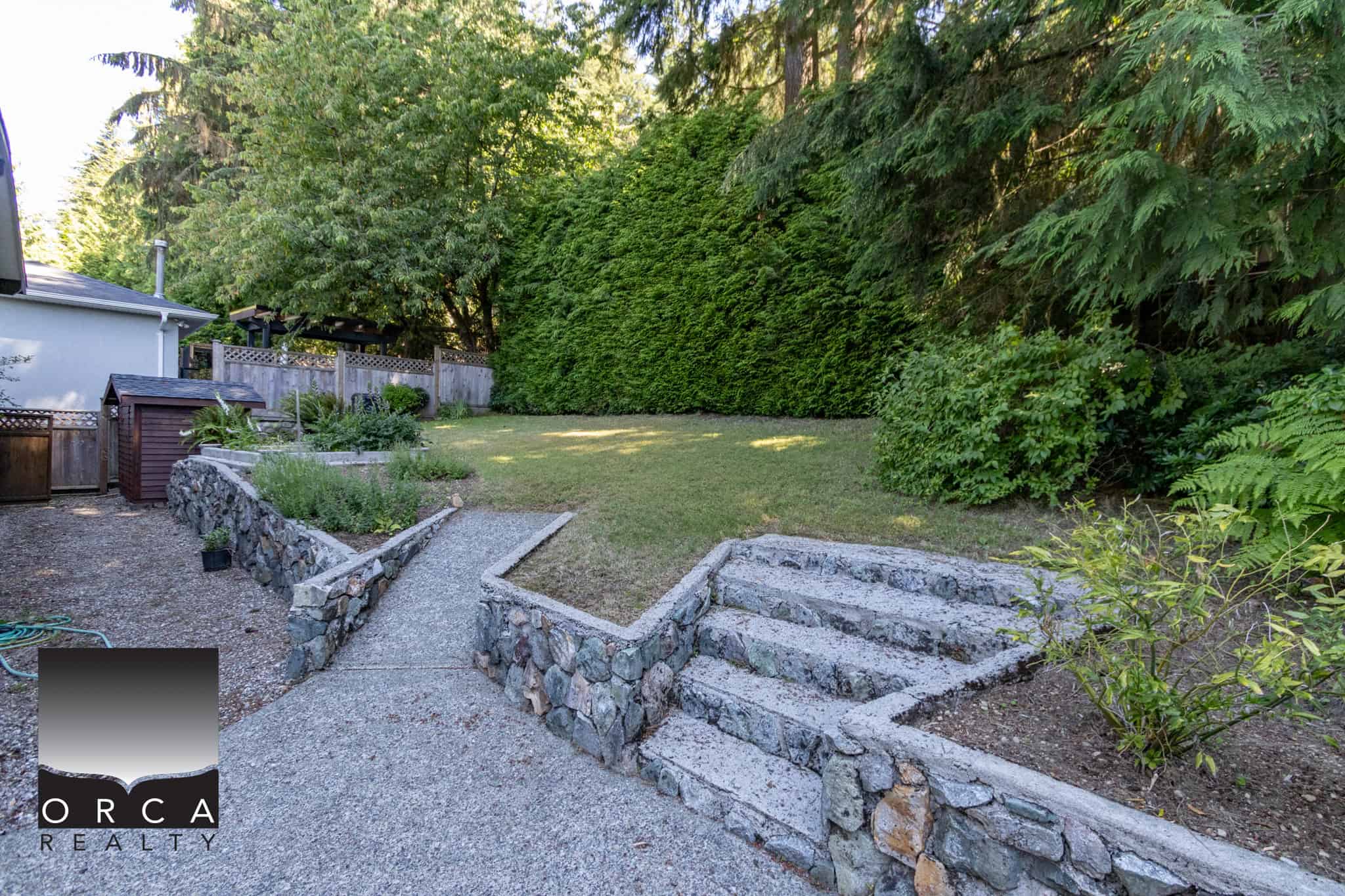 Lush backyard garden with stone terraces, well-maintained lawn, and mature trees providing privacy and serenity, ideal for outdoor living and relaxation in Victoria, BC.