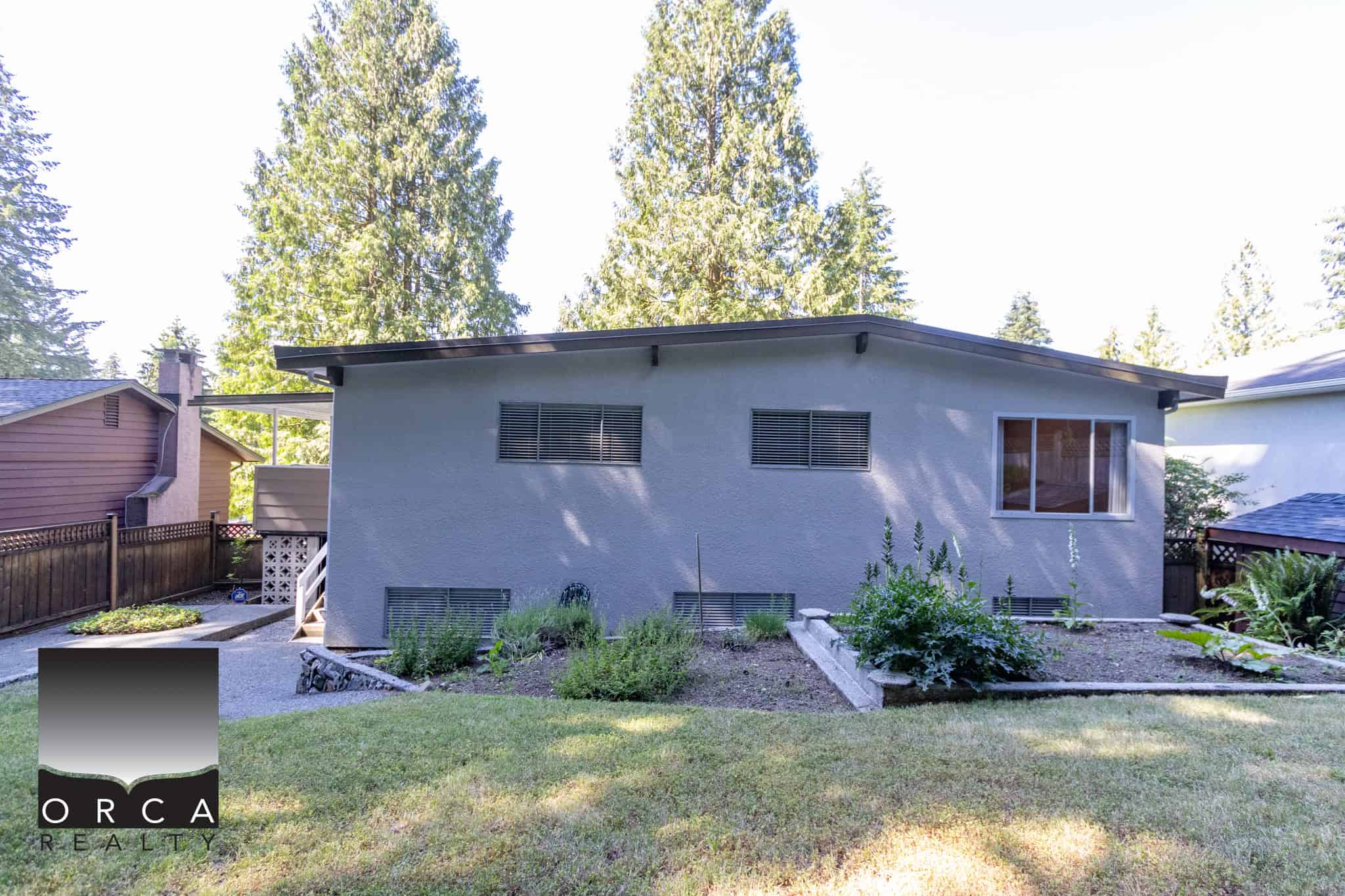 Bright backyard of a modern residential property with well-maintained garden beds, mature trees, and a wooden fence, showcasing Orca Realty Inc. services in real estate.