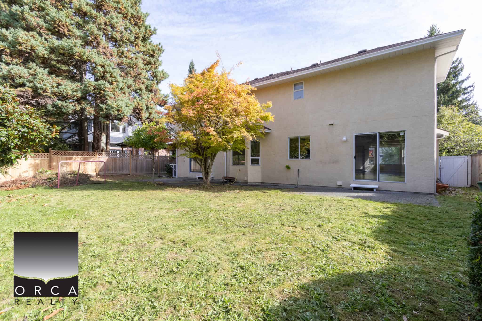Spacious backyard of a modern family home with lush green lawn, mature trees, and a cozy patio, perfect for outdoor living and entertaining.