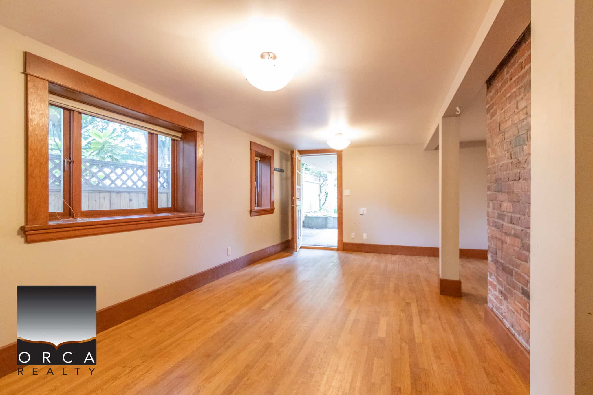 Bright living room with hardwood floors, large windows, and exposed brick accent wall, perfect for Vancouver area homes.