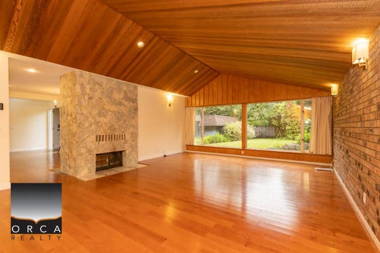 Spacious living room with large window, wooden ceiling, stone fireplace, and hardwood floors in a family-friendly home, ideal for real estate listings in Vancouver, BC.