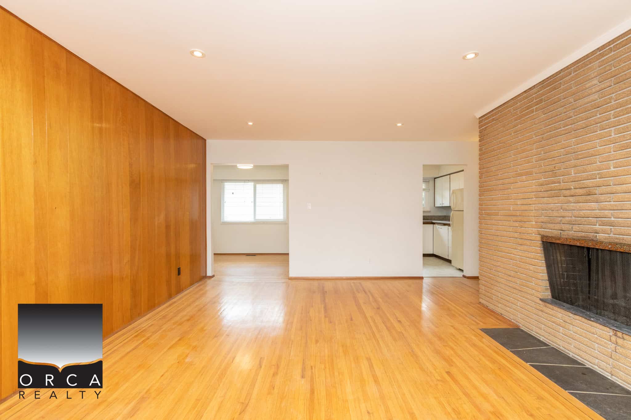 4 Bright living room with hardwood floors, brick fireplace, and large window, showcasing the comfort and style of Orca Realty Inc. homes in Victoria, BC.