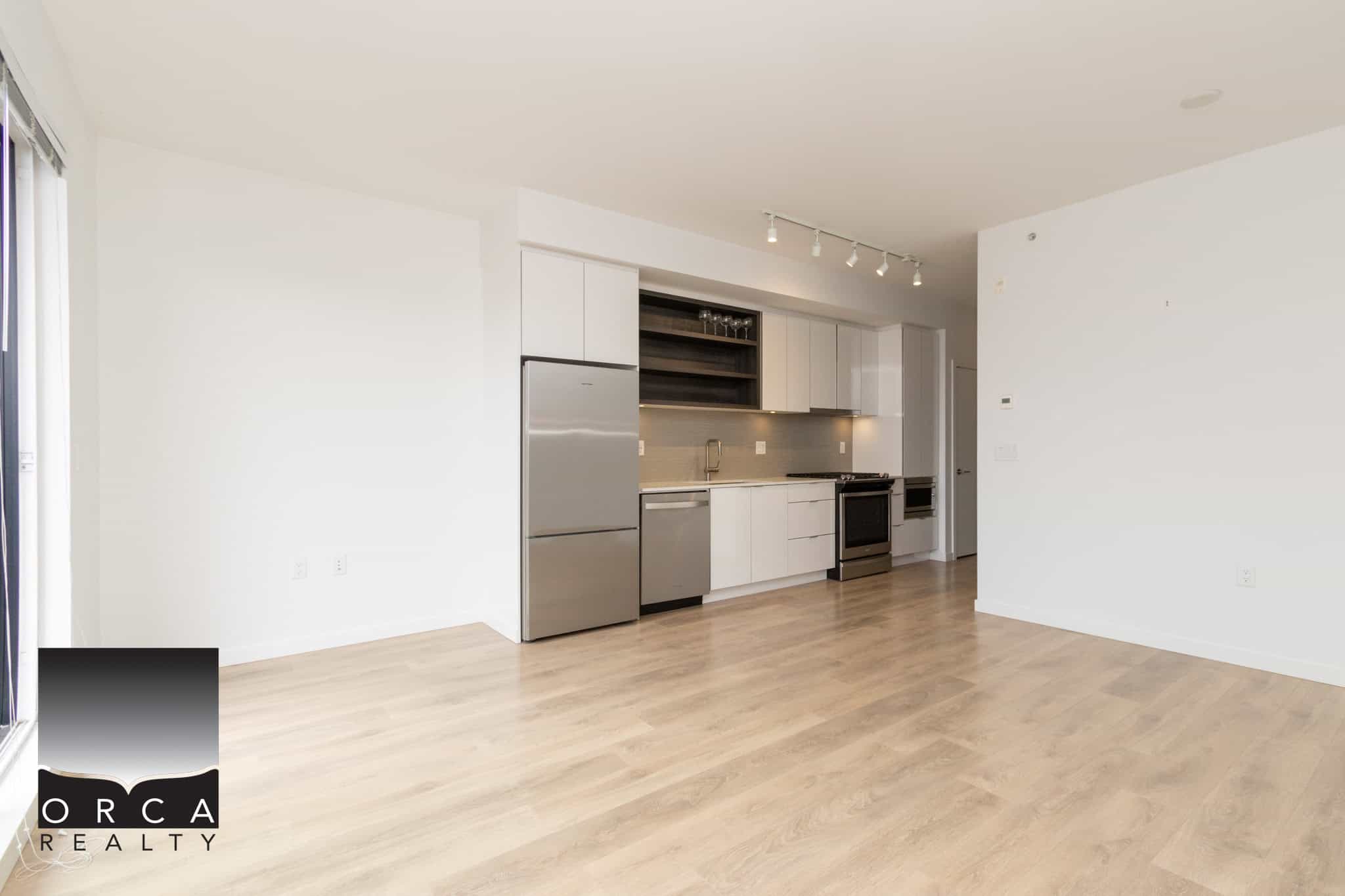 Bright modern kitchen with stainless steel appliances and minimalist white cabinetry in a spacious open-concept apartment for sale in Vancouver.