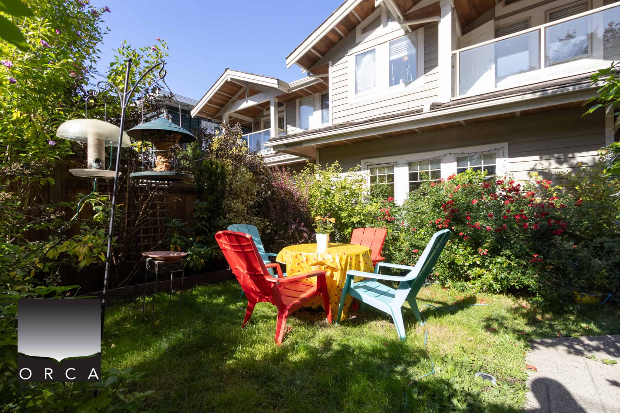 4 Bright outdoor garden patio with colorful chairs and a table, surrounded by lush greenery and blooming roses at a residential property listed by Orca Realty Inc. in Vancouver.