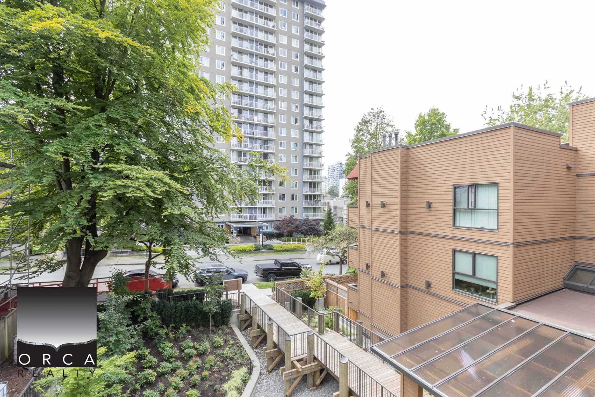 Bright city view from a modern Vancouver condo balcony with lush greenery and residential buildings.