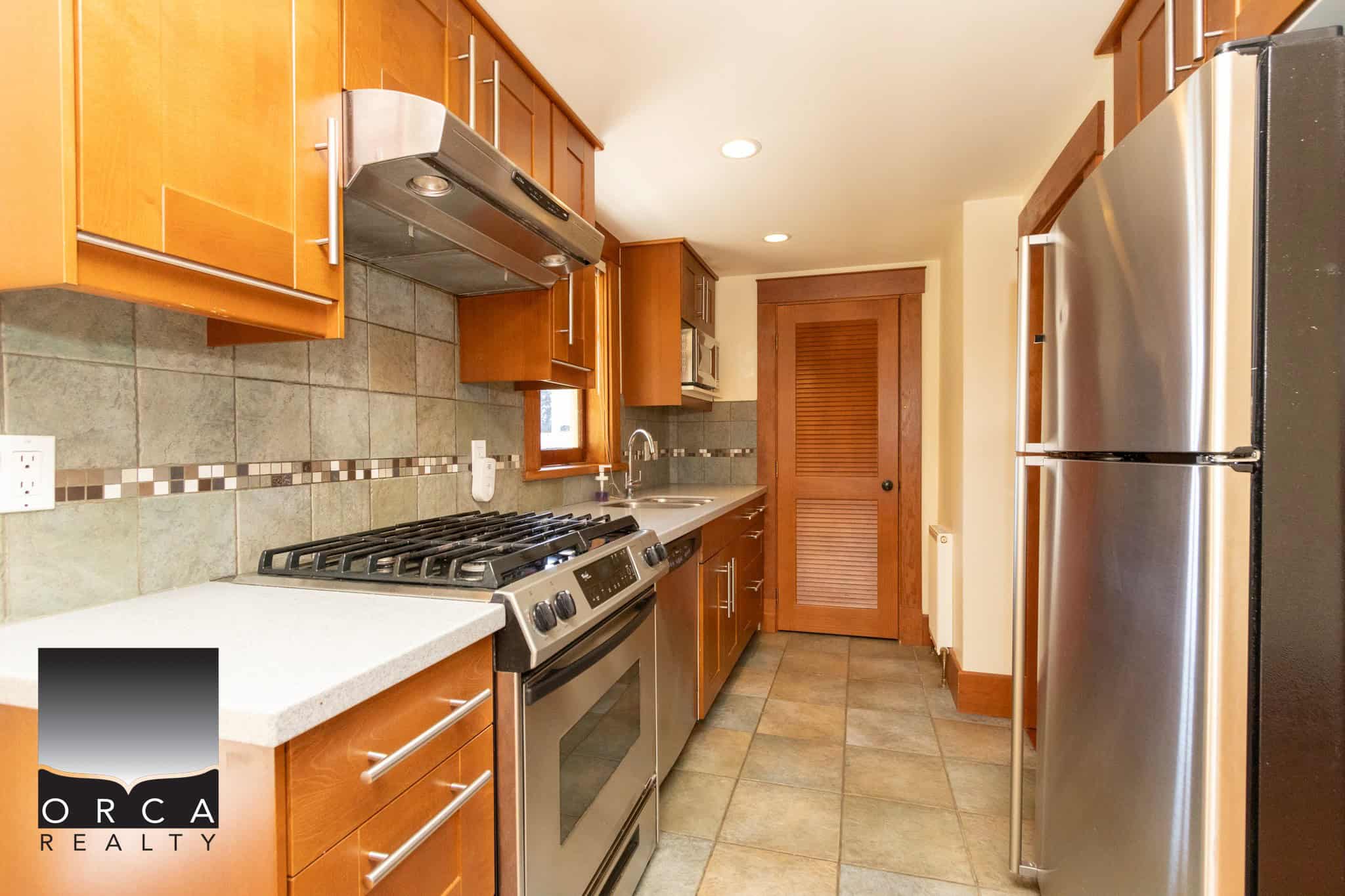 Bright modern kitchen with natural wood cabinets, stainless steel appliances, and tiled flooring, perfect for family cooking and entertaining.