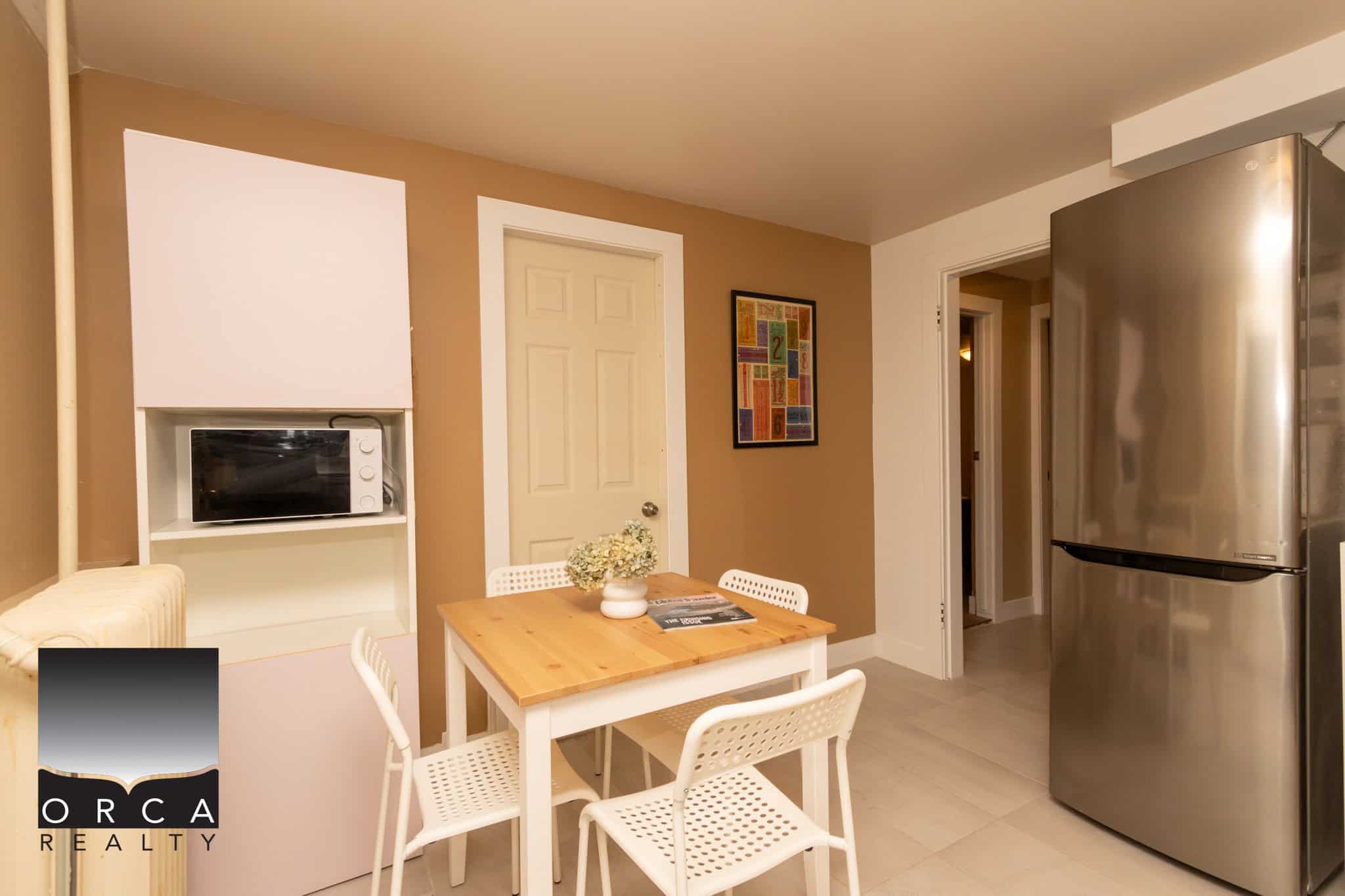 Bright & modern kitchen space featuring a sleek stainless steel refrigerator, compact microwave, and cozy dining area with white chairs, perfect for Vancouver Island living.