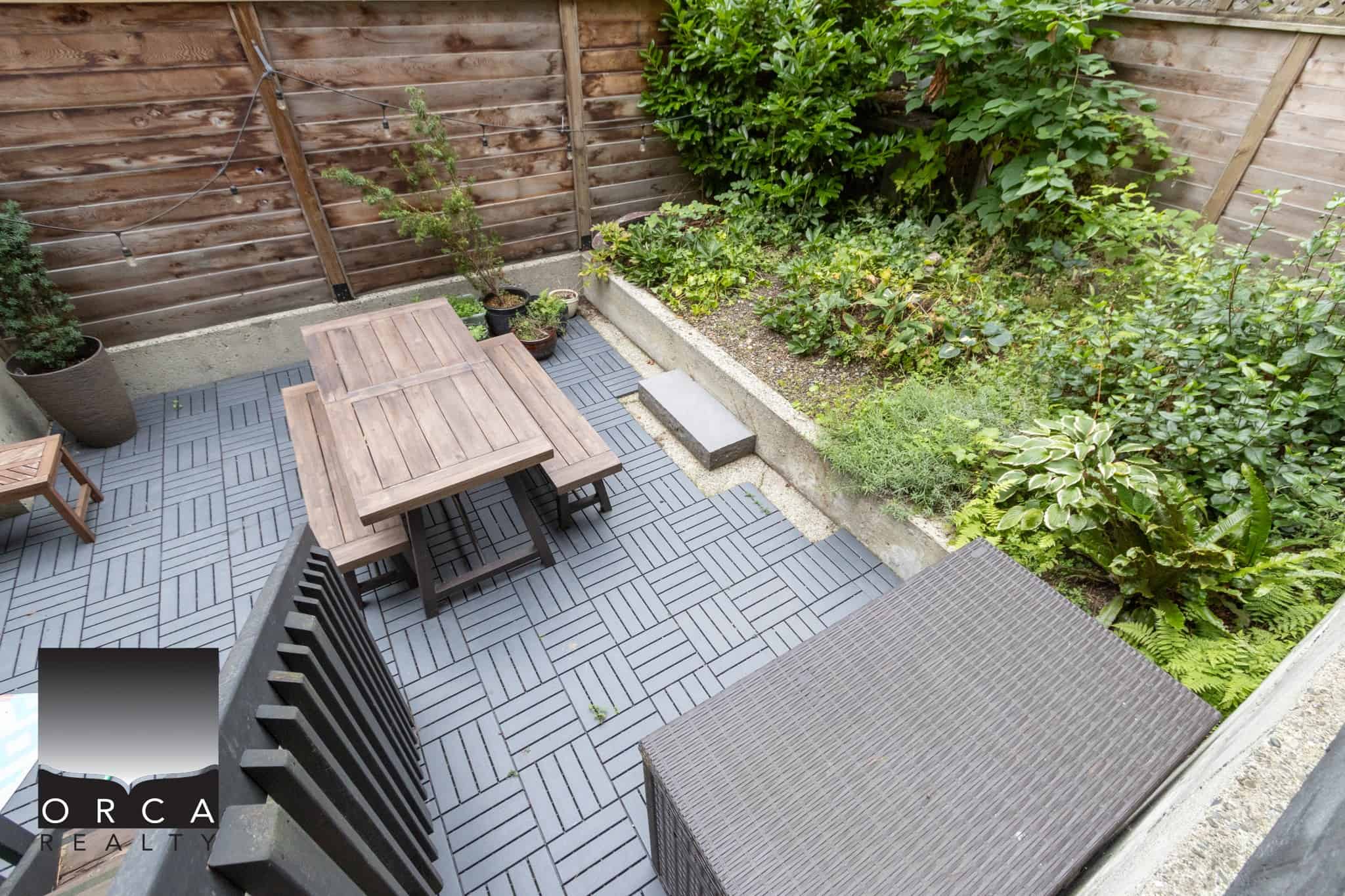 Cozy backyard patio with outdoor dining area, lush garden beds, and privacy fencing, perfect for relaxing and entertaining in a Vancouver Island home.