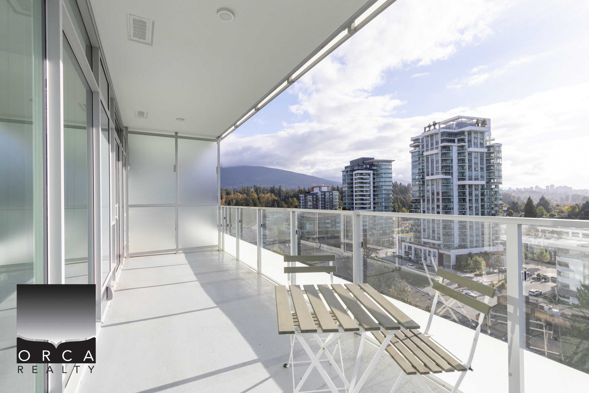 Modern balcony with glass railing showcasing cityscape and mountain views in Vancouver, BC, ideal for urban living and real estate investment.