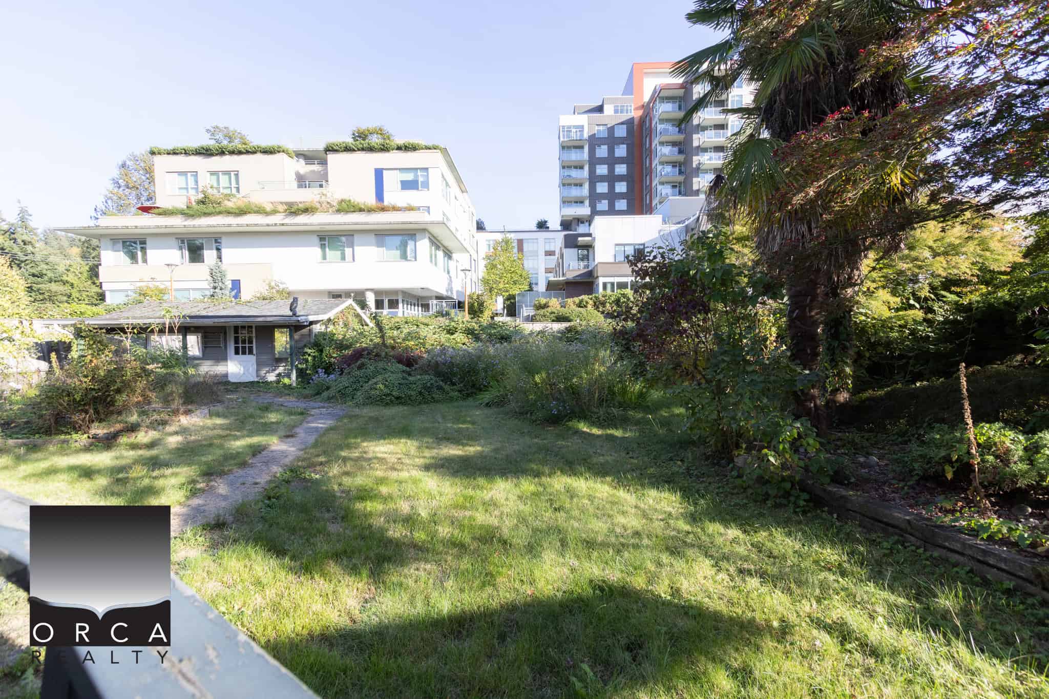 5 Lush green backyard garden with walking path and surrounding trees, close to modern high-rise condos and residential buildings in Vancouver, BC.