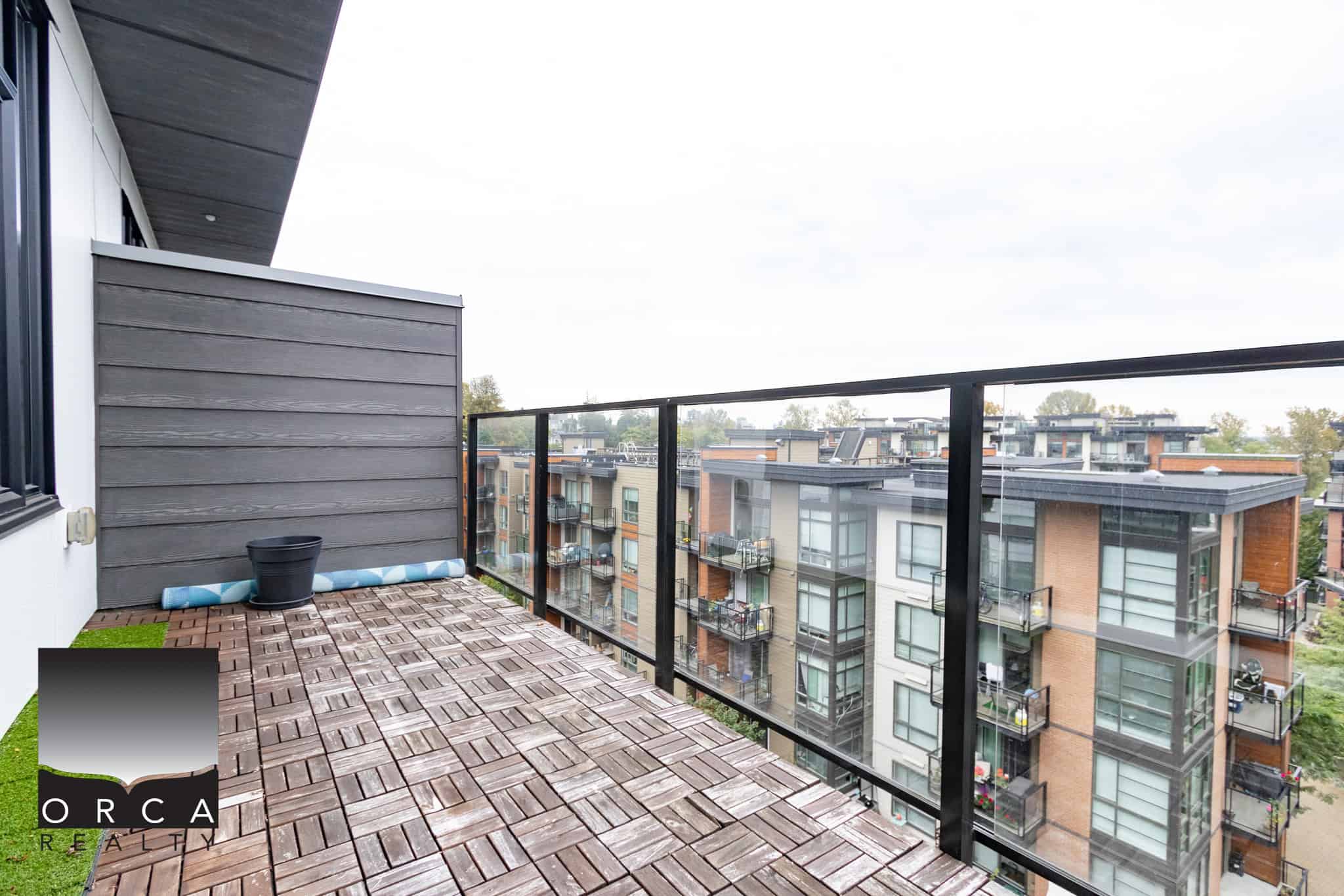 Modern apartment balcony with glass railing overlooking cityscape and surrounding residential buildings in Vancouver. Perfect outdoor space for relaxation and urban living.