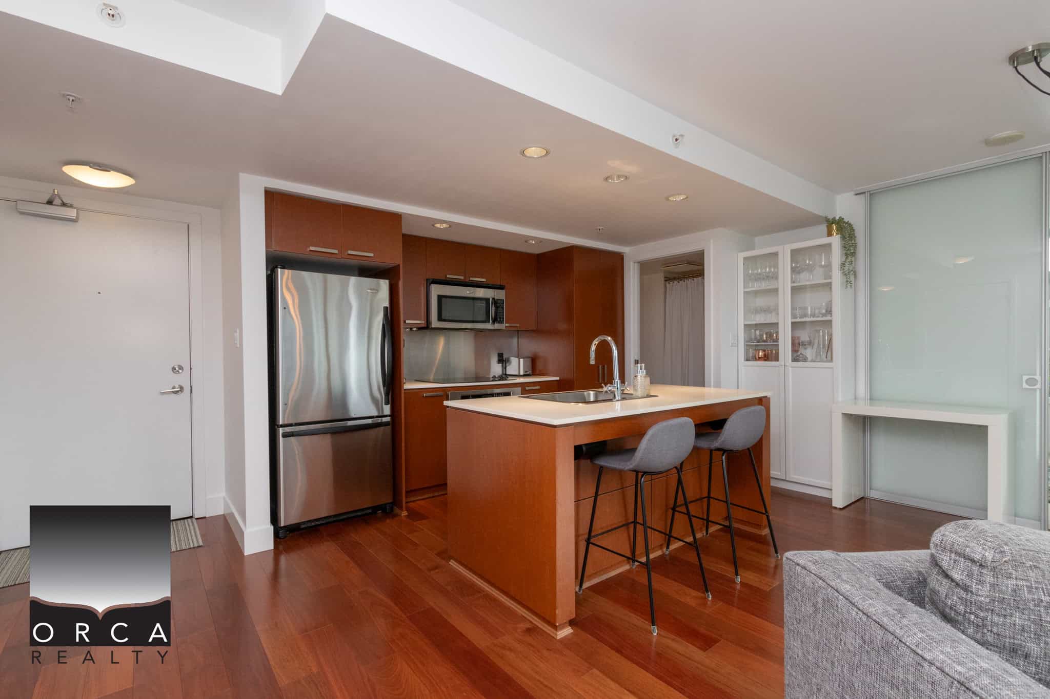 Modern open-concept kitchen with stainless steel appliances, wooden cabinetry, and a central island with bar stools, ideal for Vancouver real estate listings.