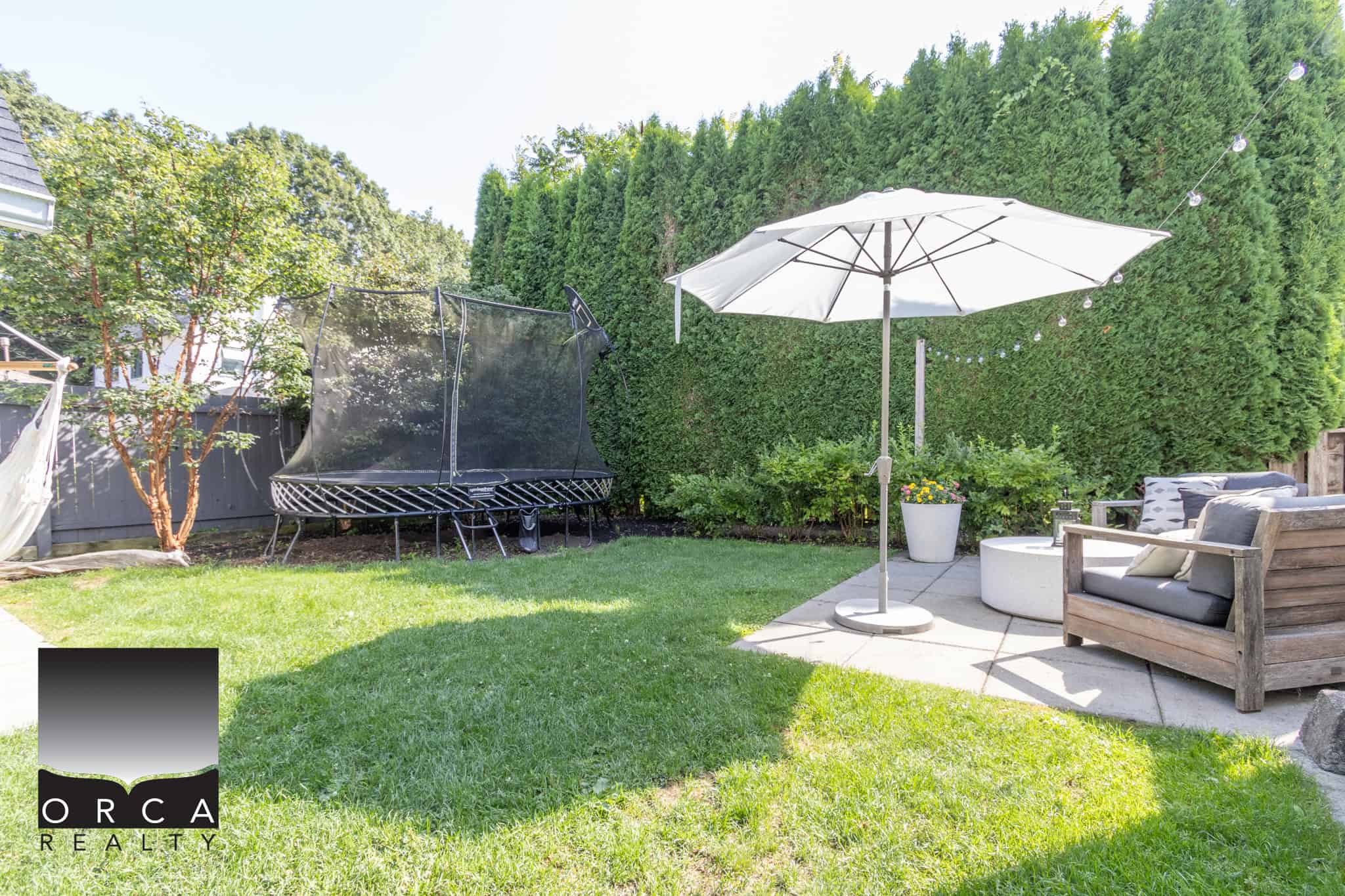 6 Spacious backyard with a trampoline, comfortable outdoor seating, large potted plants, and a shaded patio area, ideal for relaxation and outdoor entertainment in a well-maintained garden.