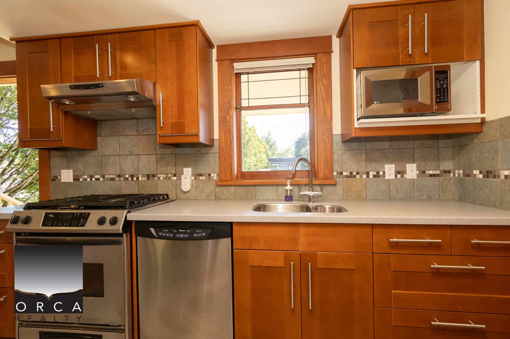 Modern kitchen with wooden cabinets, stainless steel appliances, tile backsplash, and a window with a view, offering a stylish and functional space for home cooking and entertaining.