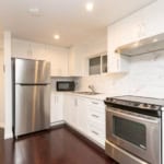 Modern white kitchen with stainless steel appliances, dark hardwood floors, marble backsplash, and bright lighting, perfect for Vancouver and BC real estate.