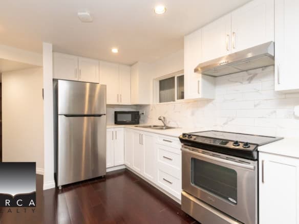 Modern white kitchen with stainless steel appliances, dark hardwood floors, marble backsplash, and bright lighting, perfect for Vancouver and BC real estate.