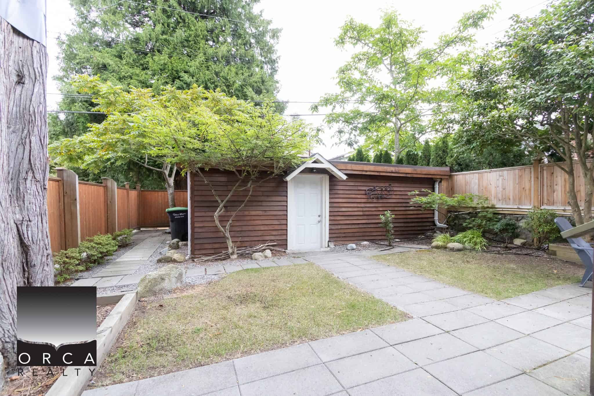 Lush backyard with a wooden shed, mature trees, and a cozy outdoor space ideal for relaxation or gardening, showcasing expert real estate services by Orca Realty Inc. in Vancouver, BC.