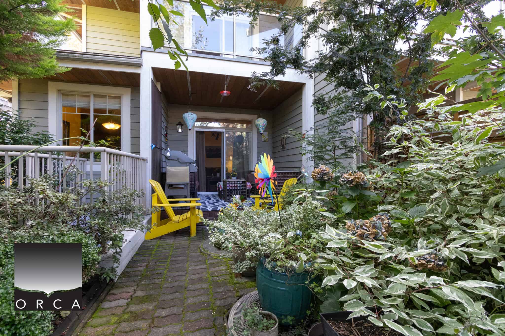 6 Colorful outdoor patio with yellow Adirondack chairs, lush greenery, and decorative lanterns, showcasing stunning real estate options from Orca Realty Inc. in Victoria, BC.