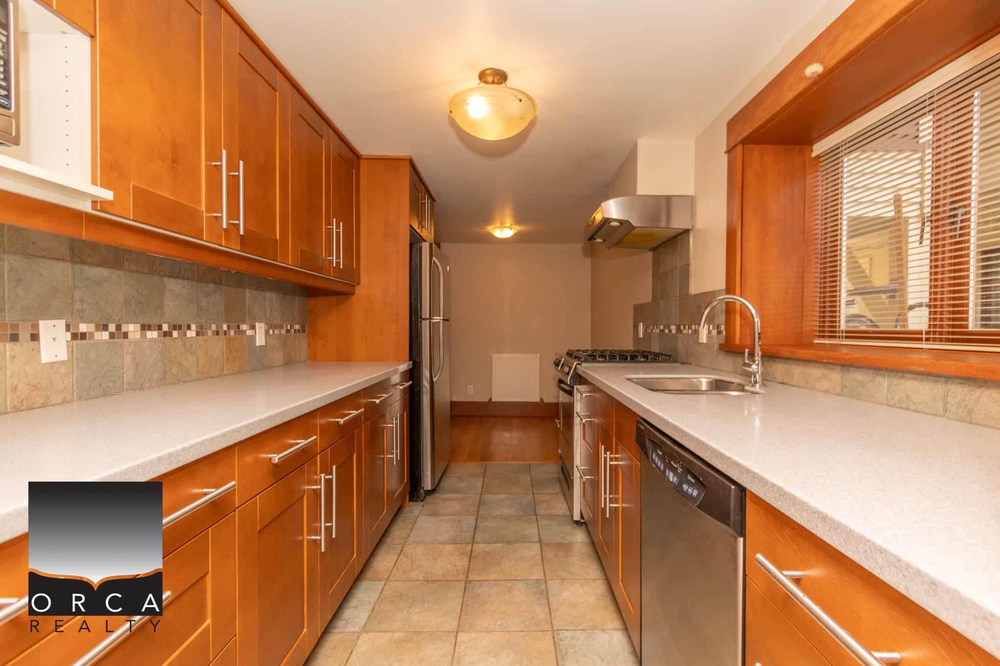 Bright modern kitchen with wooden cabinetry, stainless steel appliances, and ceramic tile flooring, ideal for Vancouver Island homebuyers seeking stylish and functional culinary spaces.