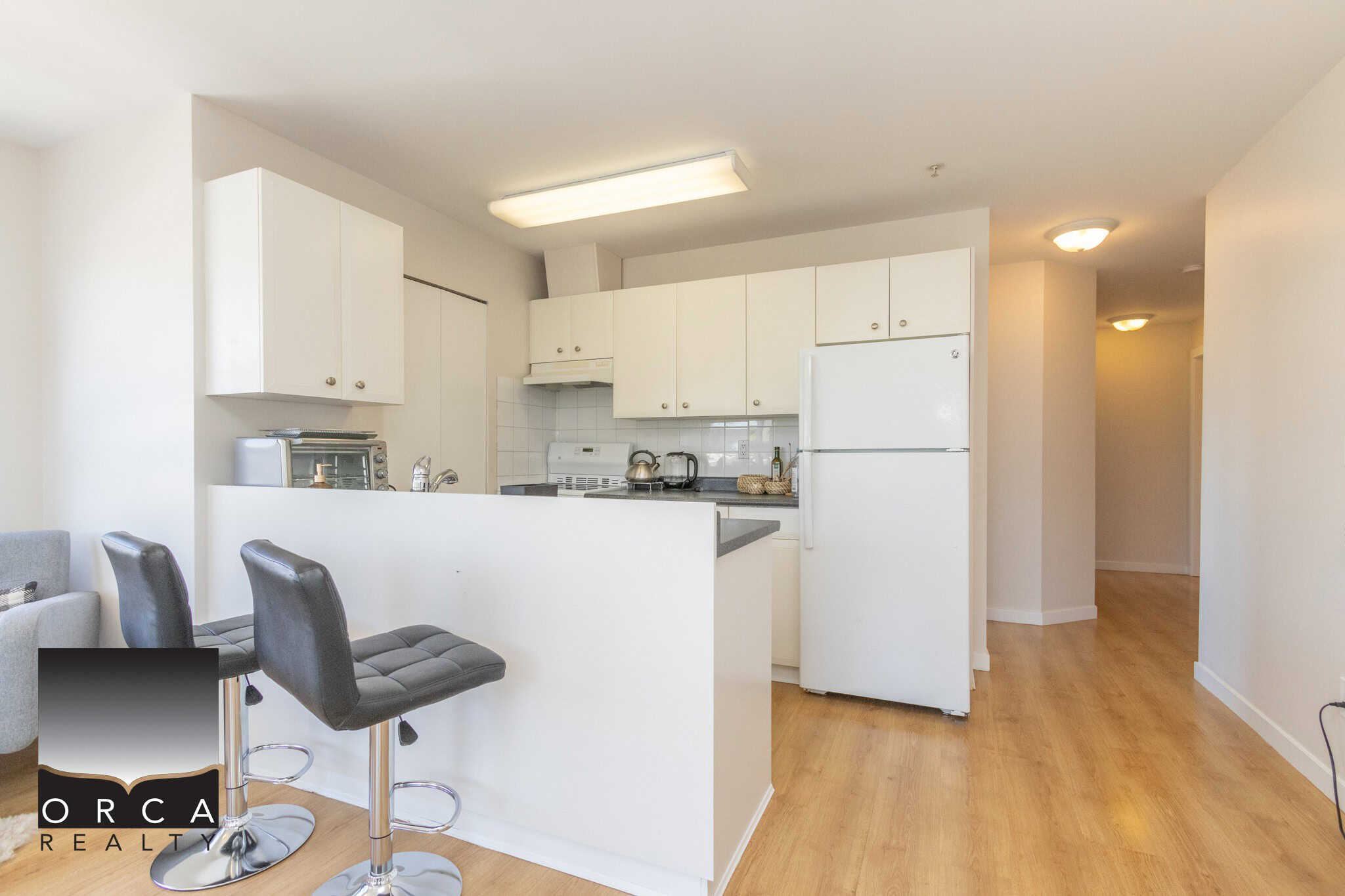 Modern kitchen with white cabinets, appliances, and breakfast bar in an Vancouver-area condo listing, ideal for homebuyers seeking contemporary condo living in BC.