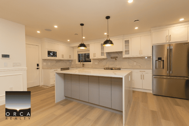 Spacious modern kitchen with white cabinetry and stainless steel appliances, including a large refrigerator and island counter, ideal for Vancouver real estate buyers.