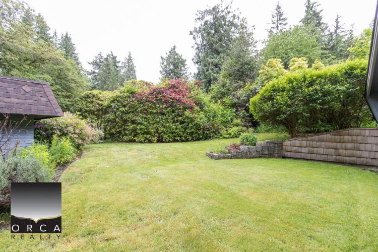 Lush green backyard with well-maintained lawn, mature trees, and garden shrubs, ideal for outdoor living and relaxation in Victoria, British Columbia.
