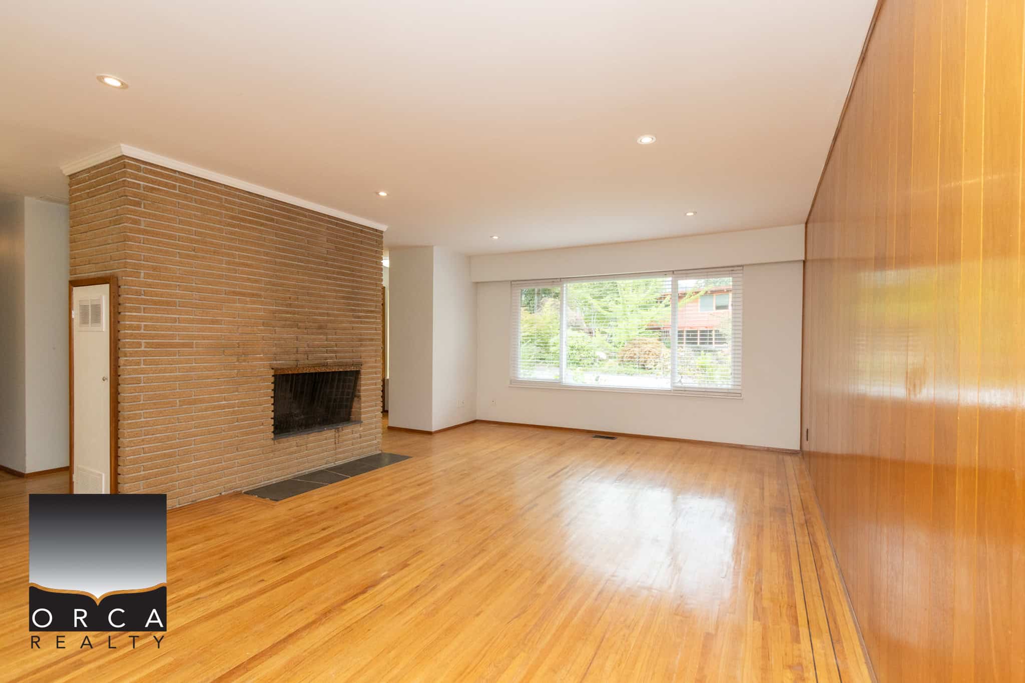 7 Spacious living room with hardwood flooring, brick fireplace, large window providing natural light, ideal for Vancouver real estate buyers.