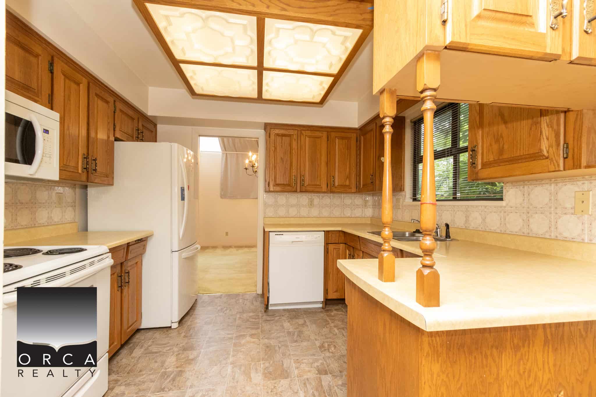 Bright kitchen with oak cabinets, white appliances, and beige countertops, showcasing a cozy home interior perfect for families or first-time buyers.
