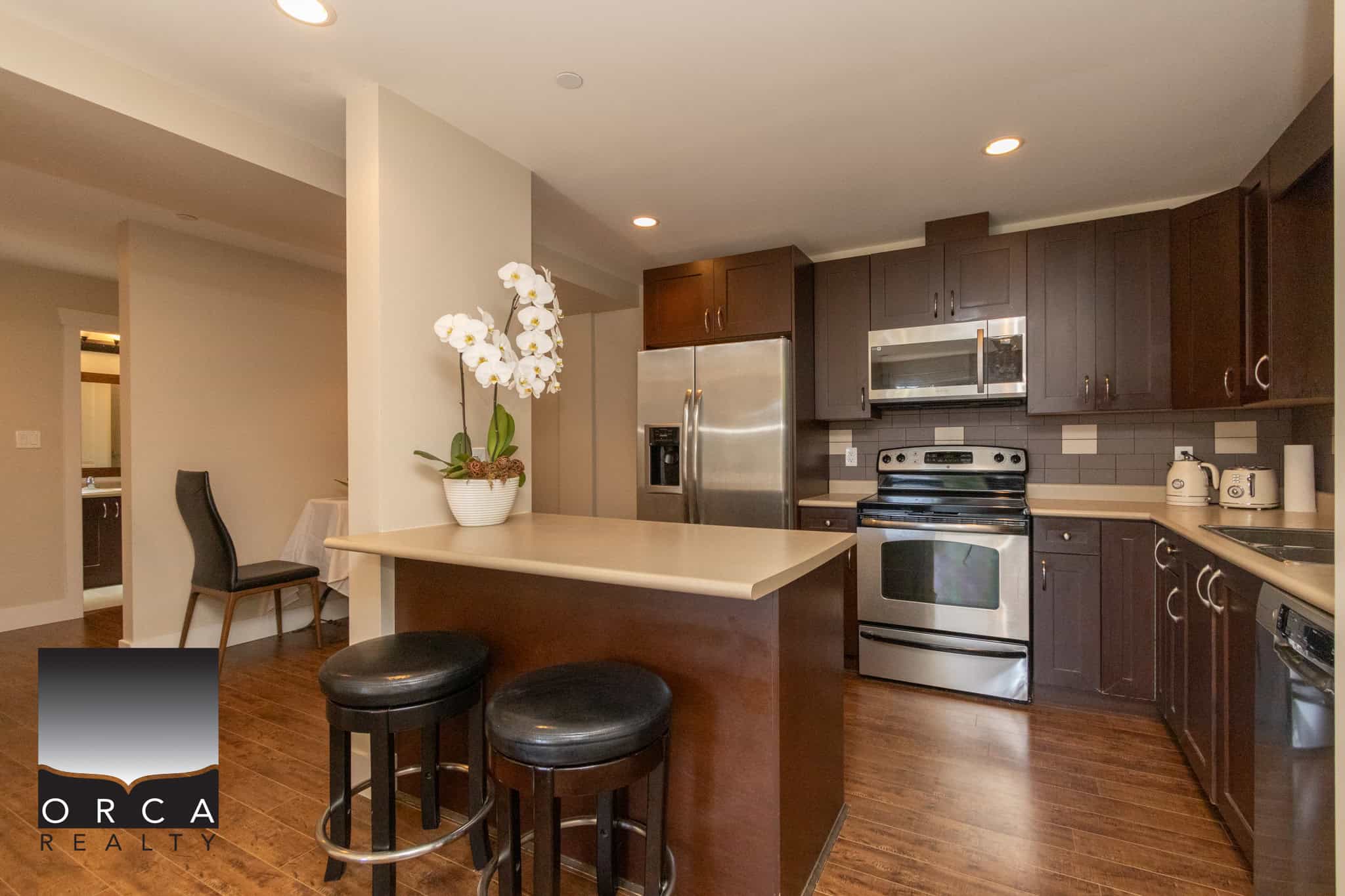 Modern kitchen with stainless steel appliances and dark wood cabinets, featuring a breakfast bar and cozy dining area, perfect for Vancouver Island homes.