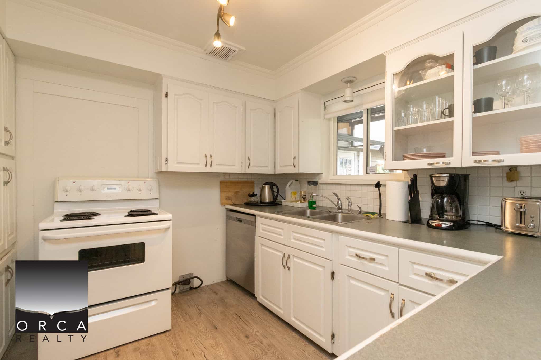7 White kitchen with white cabinets, stove, sink, coffee maker, and kitchenware, modern home interior, Orca Realty Inc., Vancouver real estate listing.