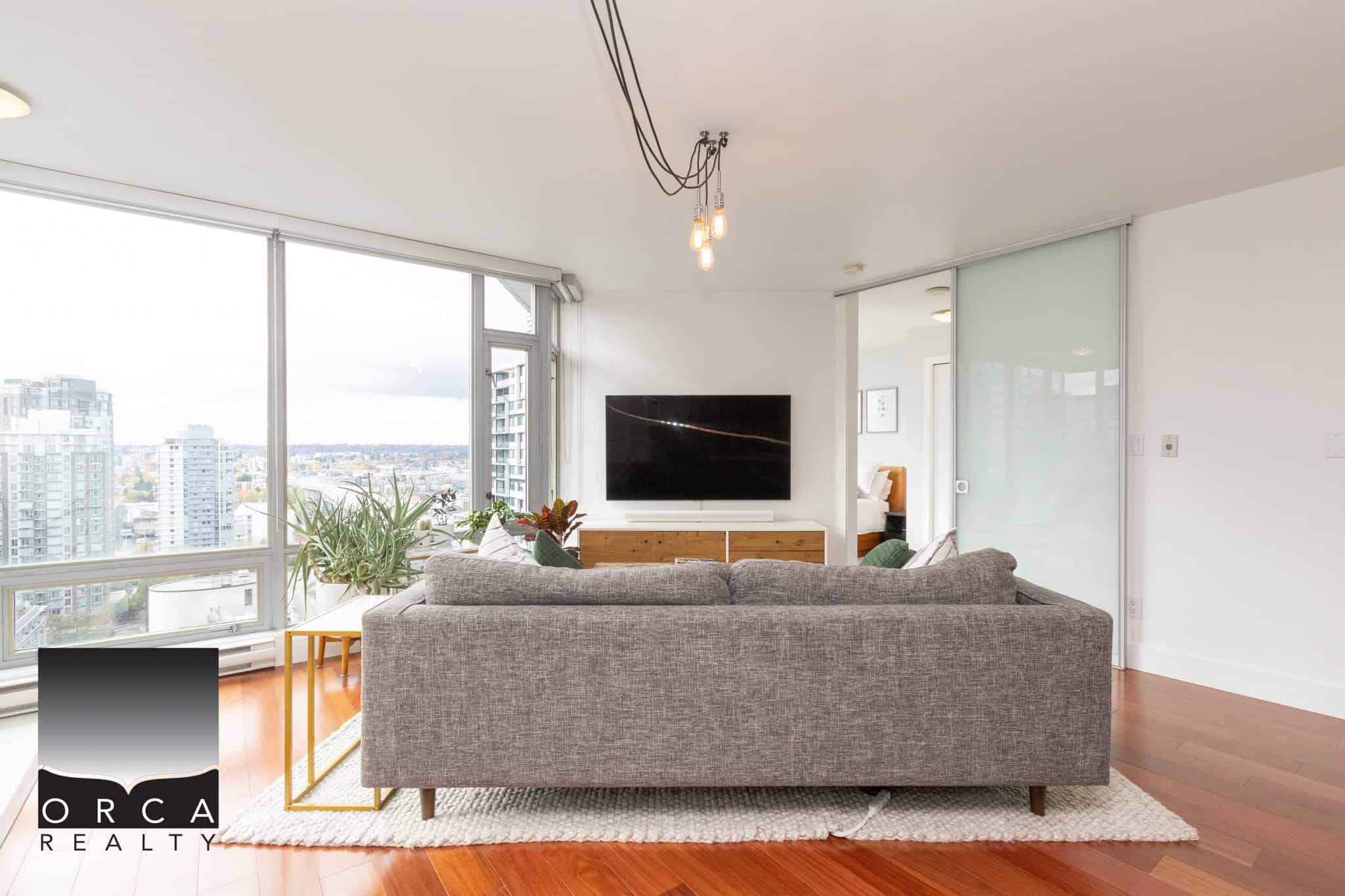 Modern urban living room with large windows, city skyline views, contemporary furniture, hardwood floors, and minimalist decor, ideal for Vancouver real estate.