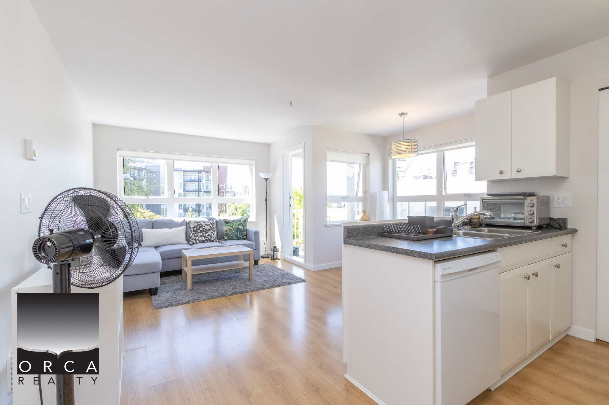 Bright and spacious Vancouver apartment living room with modern decor, large windows, and open kitchen, showcasing a comfortable living space ideal for tenants and buyers.