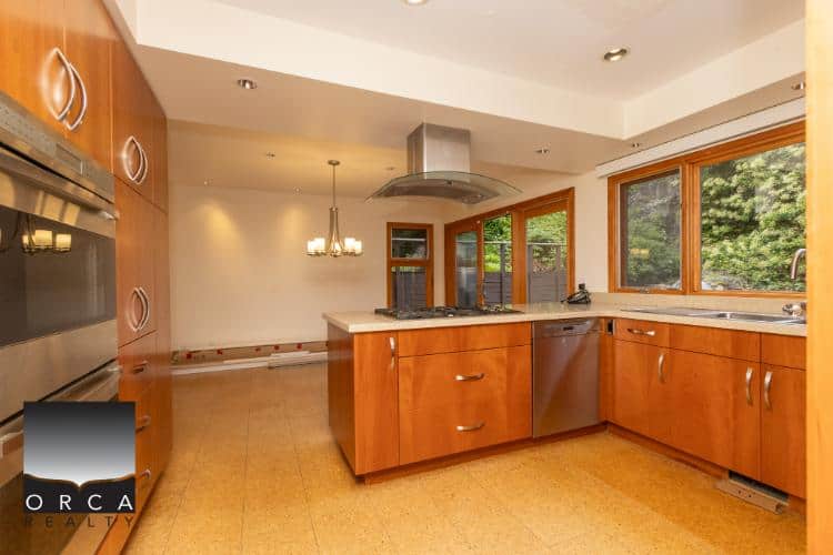 Modern kitchen with maple cabinets, stainless steel appliances, large windows showcasing greenery, and updated countertops, ideal for Vancouver Island real estate listings.