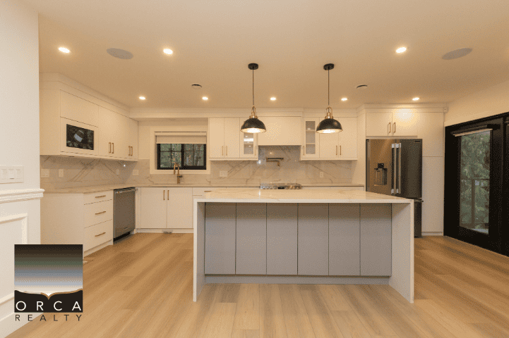 Modern kitchen with white cabinetry, stainless steel appliances, hardwood flooring, and ample natural light, showcasing Orca Realty's exceptional property listings in BC.