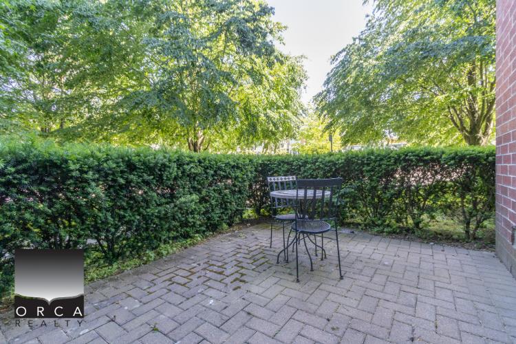 A small outdoor patio with a metal table and chairs surrounded by lush greenery and well-maintained hedges, ideal for relaxation and outdoor dining in a peaceful residential setting.