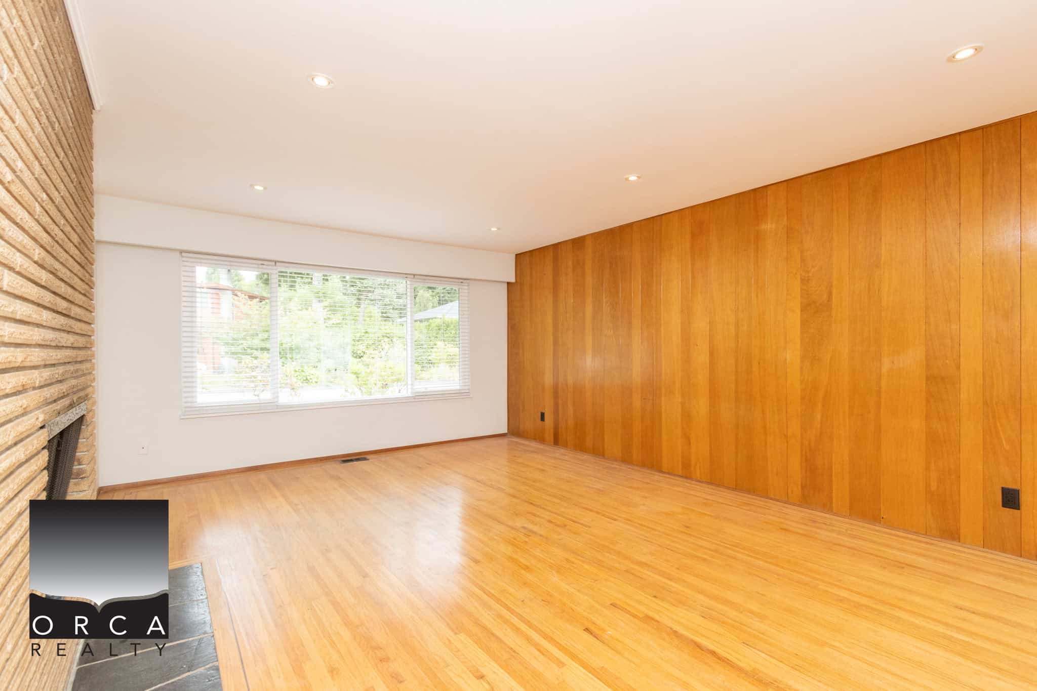 8 Spacious living room with large window, hardwood floors, and wood-paneled accent wall, perfect for Vancouver home buyers seeking modern real estate.