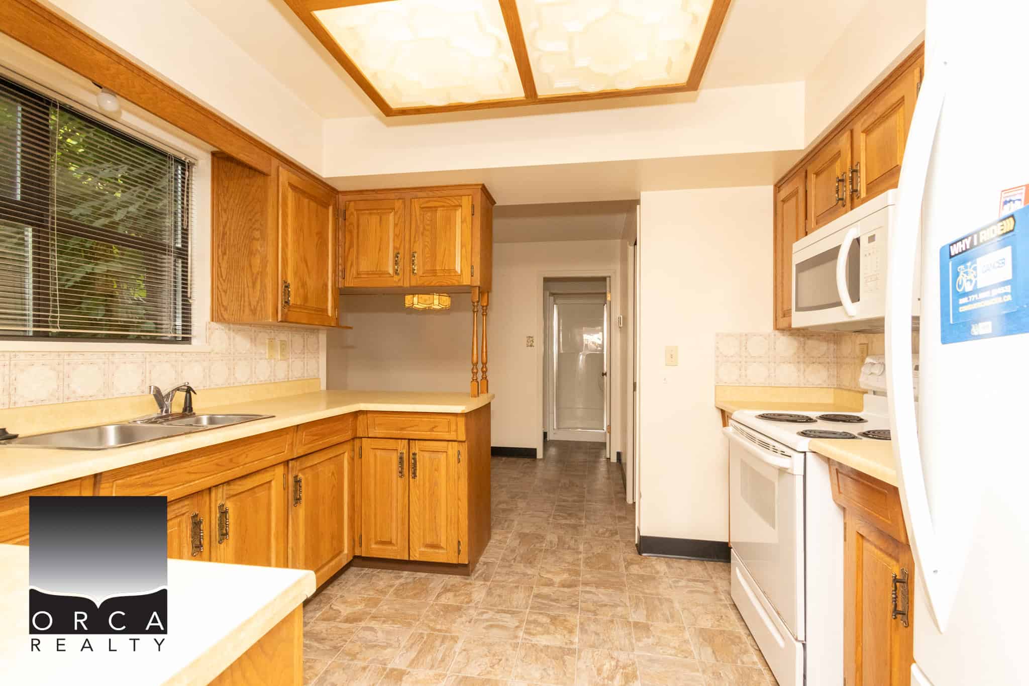 Bright kitchen with wooden cabinetry, white appliances, laminate flooring, and natural light from a window, offering a welcoming space for home cooking and living in Vancouver Island.