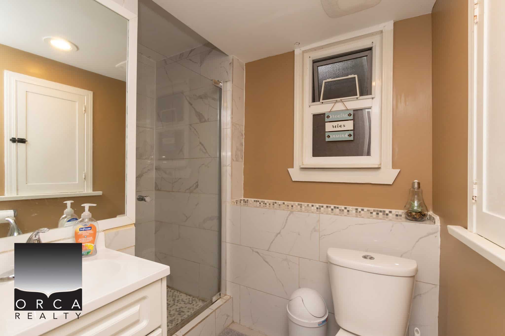 Modern beige bathroom with marble accents, walk-in shower, and decorative window, showcasing home comfort and style - ideal for real estate listings.