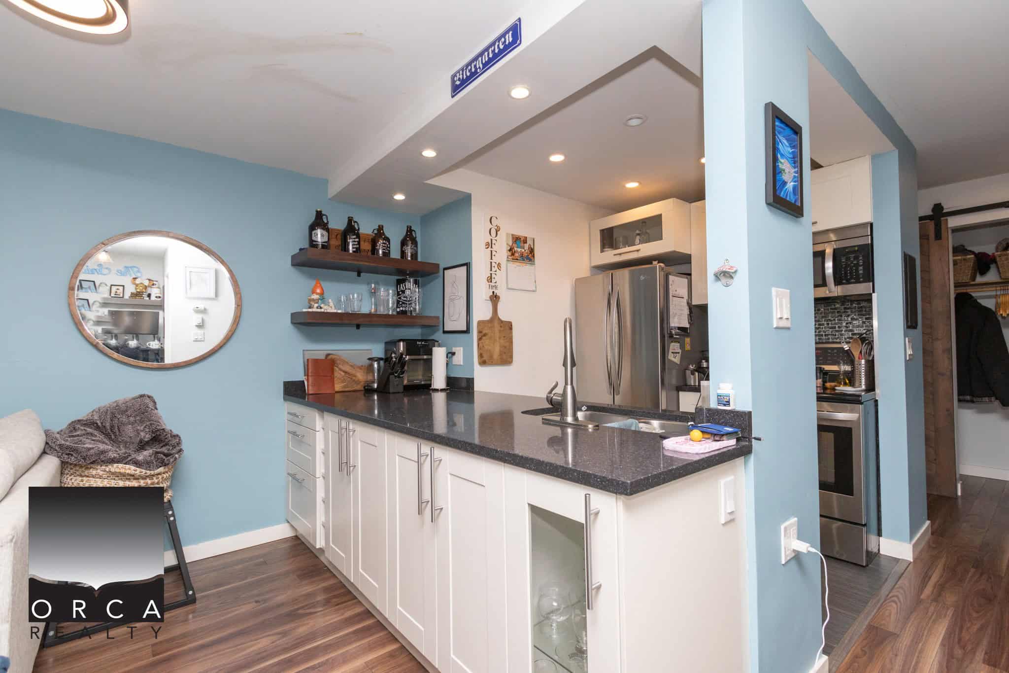 Modern kitchen with stainless steel appliances and white cabinetry, featuring a black granite countertop and light blue walls; ideal for Vancouver Island real estate listings.