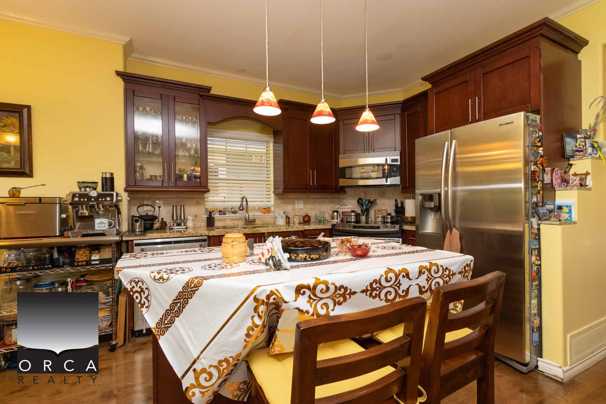 8 Modern kitchen with dark wood cabinets, stainless steel appliances, and a large dining table covered with a decorative tablecloth, perfect for family meals and entertaining.