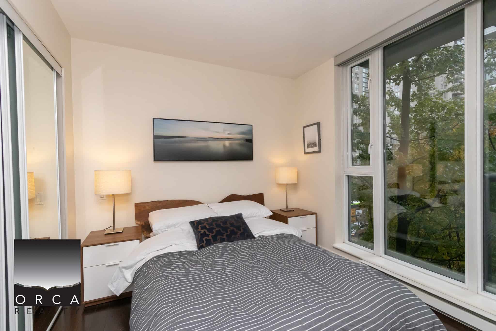 Comfortable modern bedroom with large windows overlooking greenery, stylish bedding, and minimalist decor, ideal for urban Vancouver living.