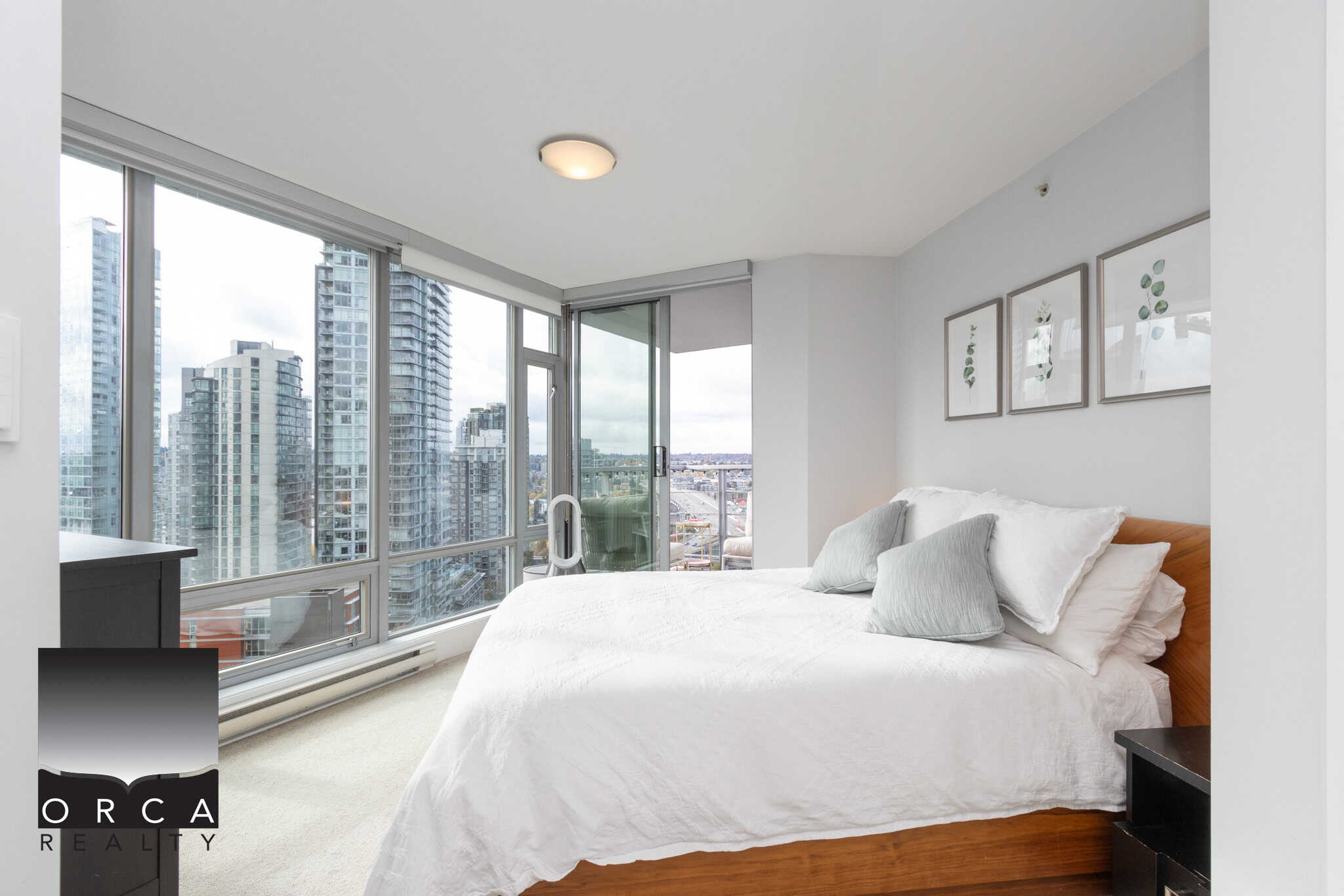Modern high-rise bedroom with floor-to-ceiling windows providing panoramic city views, featuring a cozy bed with neutral linens in Vancouver's downtown real estate market.
