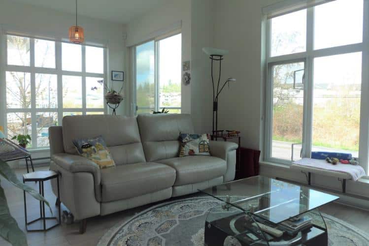 Bright living room with large windows and modern furniture, showcasing Vancouver Island real estate listings with cozy and stylish interiors.