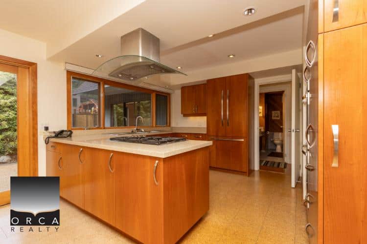 Modern kitchen with cherry wood cabinets, stainless steel appliances, and large windows showcasing nature views. Perfect for Vancouver area homeowners seeking stylish and functional real estate options.