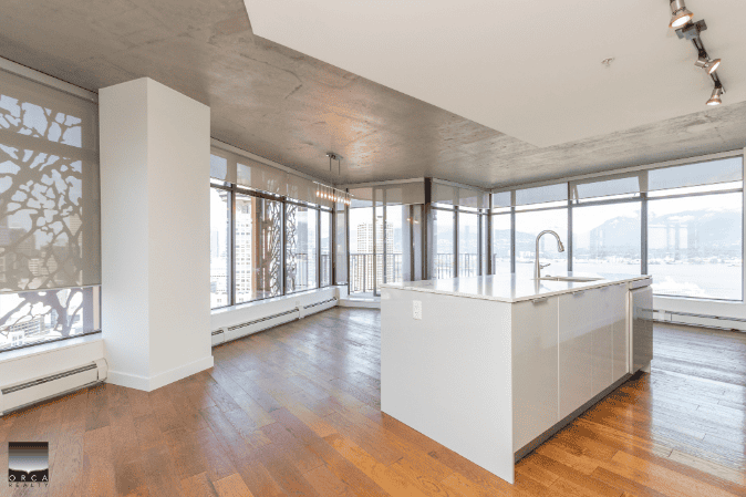 Spacious modern condo interior with panoramic city and water views, featuring large windows, hardwood flooring, and an open plan kitchen, ideal for luxury living in Vancouver.