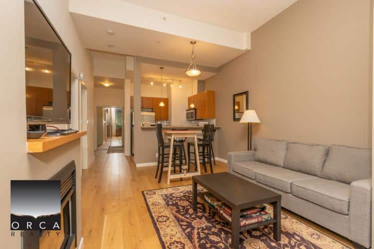 Modern Vancouver-style condo living room with open kitchen, hardwood floors, and comfortable seating, perfect for buyers searching for downtown condo apartments in Vancouver by Orca Realty Inc.