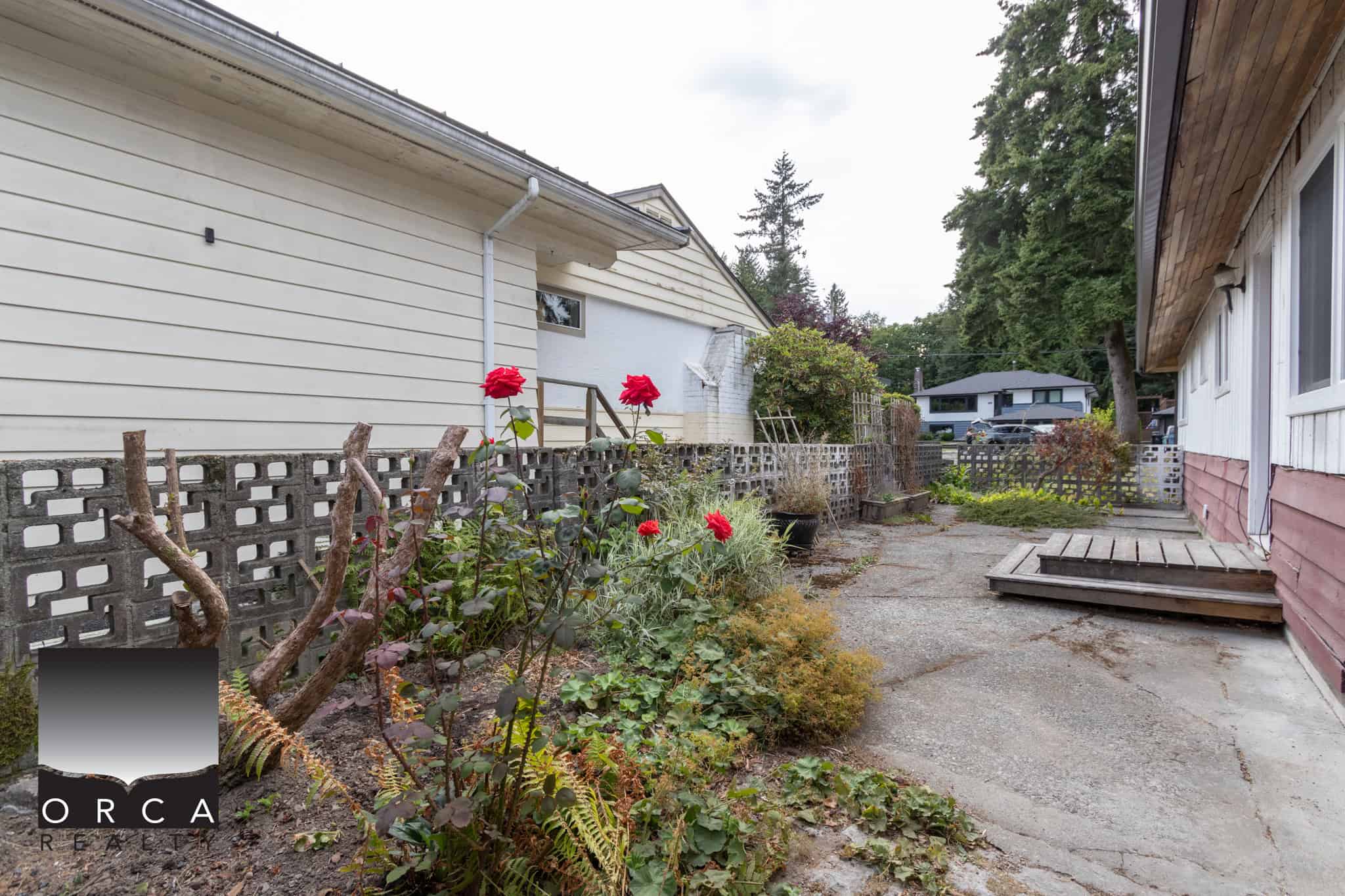 9 Rustic backyard with concrete patio, flower garden, and wooden stairs, featuring a cozy residential property in Vancouver, BC, ideal for Vancouver homebuyers seeking outdoor spaces.